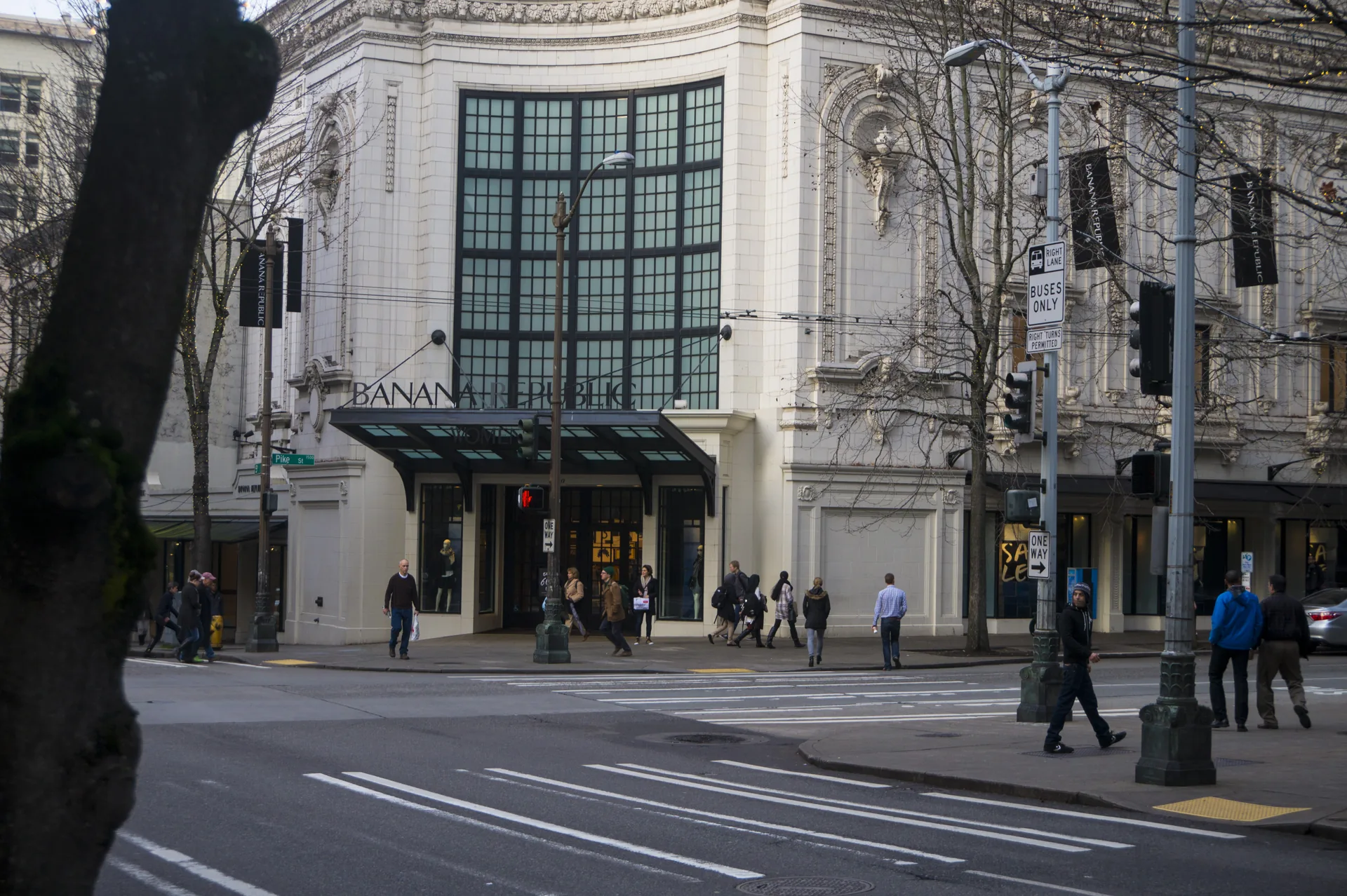 An ornate cream-coloured corner building with a tall arched window and an awning lettered “Banana Republic”, pedestrians walking past wide crosswalks and bare trees.
